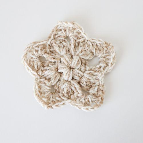 a flat lay image of a crochet star made holding two strands of yarn together, a cream and a sparkly DK to show how this pattern looks using this technique.