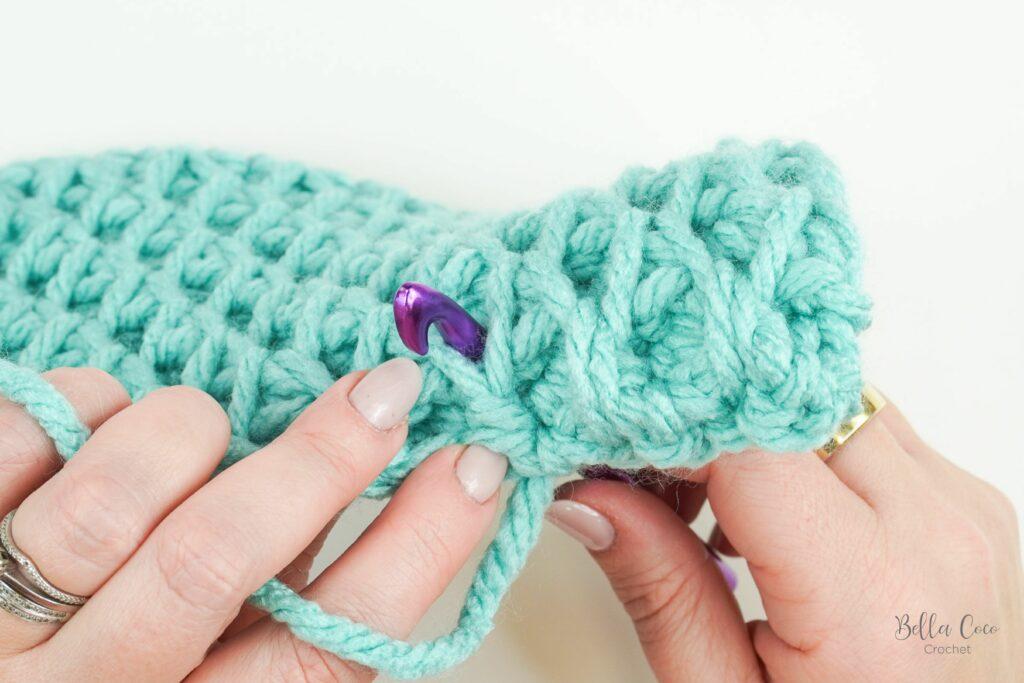 yarn swatch of honeycomb stitch using aqua yarn and purple crochet hook. image indicates where to insert hook
