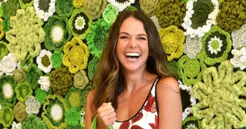 a photograph of a woman standing in front of a crochet flower wall.