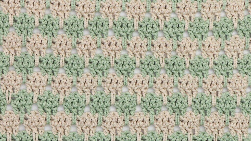 Close-up of crochet larksfoot stitch pattern in alternating rows of sage green and cream yarn. The stitch design features vertical elongated loops resembling bird footprints, creating a textured, repeating geometric pattern.