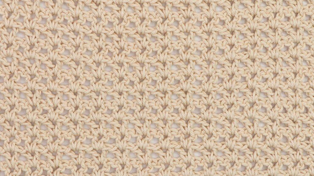 Close-up of a beige crochet swatch using the V-stitch, showing a lacy and open texture with a repeating V-shaped pattern.