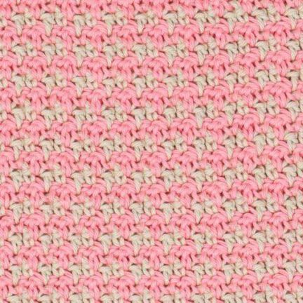 Close-up of a pink and cream crochet swatch demonstrating the houndstooth stitch pattern, showing a repeating, textured design made with alternating colours.