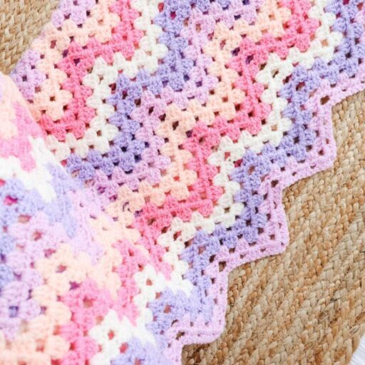 A granny ripple blanket with pink, fuchsia, white, purple and peach stripes.