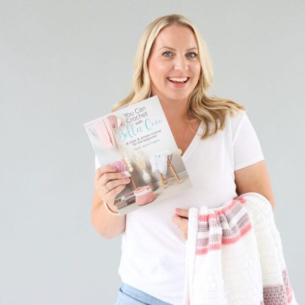 Bella Coco Book Sarah-Jayne from Bella Coco stood infont of a grey background with a crochet blanket draped over her arm whilst holding her new book in the opposite hand.