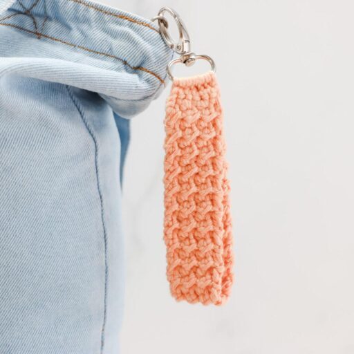 Keychain on a denim bag made from orange crochet on silver hardware.